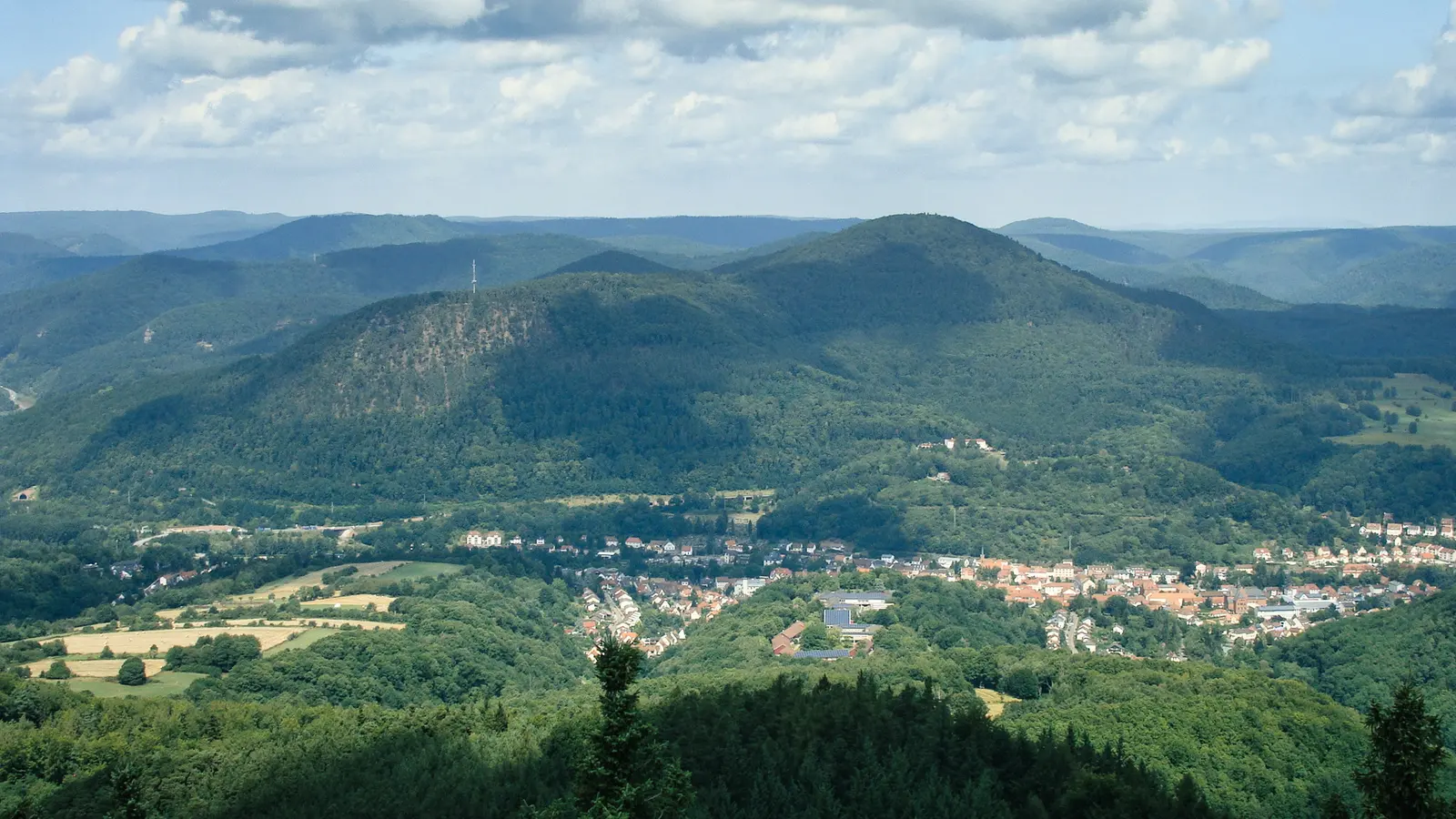 Blick über bewaldete Hügel des Pfälzerwalds auf ein Dorf im Tal